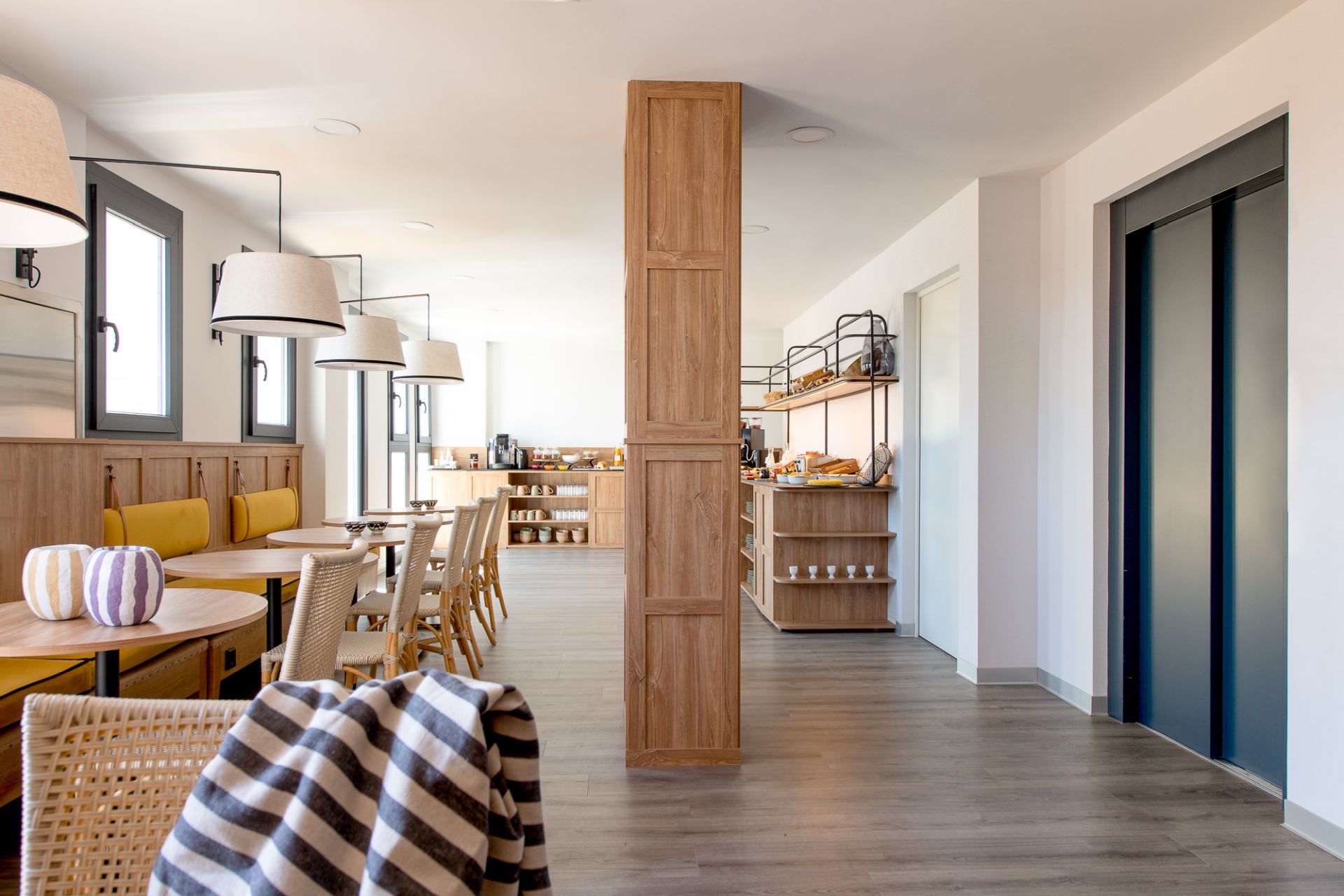 Zona de comedor de hotel reformada con pilar de madera y lámparas colgantes